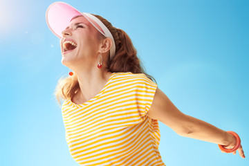 smiling active woman in yellow shirt against blue sky rejoicing