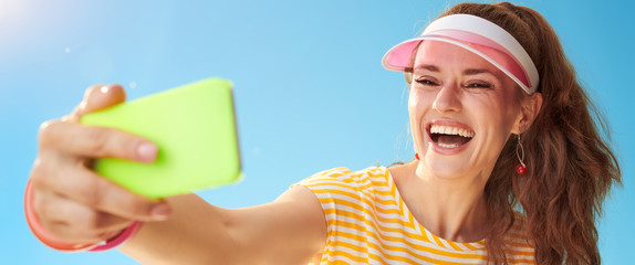 happy young woman against blue sky taking selfie with phone