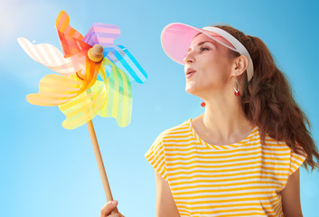smiling fit woman against blue sky blowing on colorful windmill
