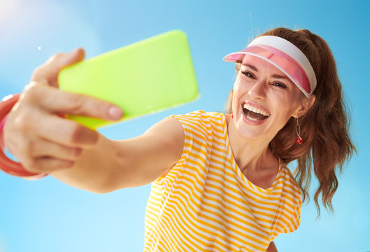 happy young woman against blue sky taking selfie with cellphone