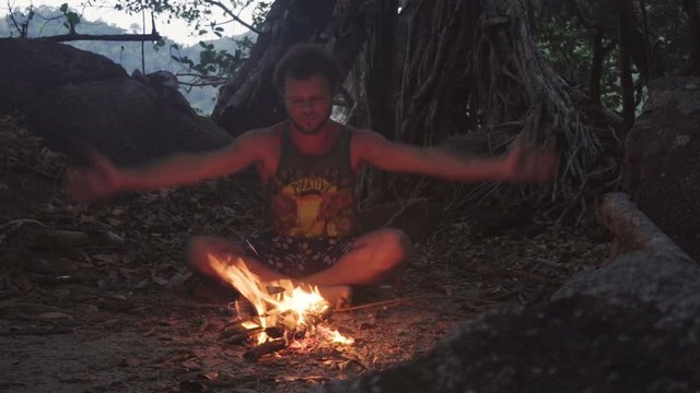 Caucasian Man Burning Little Campfire in the Tropical Forest at Twilight to Boil Kettle with Rice for Dinner. Ritual Shamanism Dancing Around the Fire.