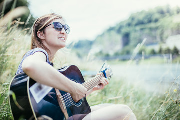 Junges Mädchen sitzt in der Wiese und spielt Gitarre, Singen