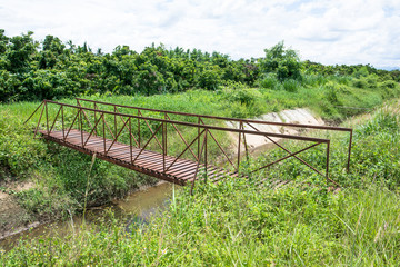 Old metal bridge at irrigation canal with tree and sky background