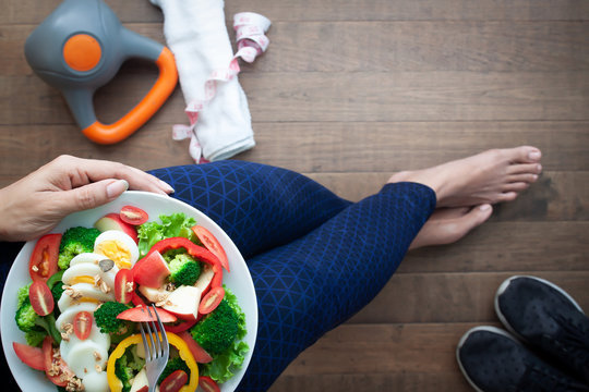 sporty woman eating egg salad with broccoli, Fitness equipments on floor. Directly above, healthy lifestyle concept