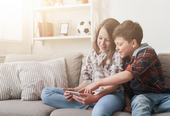 Two kids playing on smartphone on sofa at home