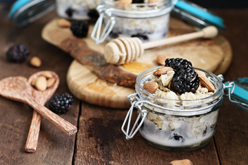 Overnight oatmeal with blackberries, honey and almond milk on a rustic wood background in a canning glass bail jars with attached lid. Selective focus on oatmeal in front.