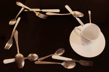a frame of cutlery and a cup and a saucer on a dark background