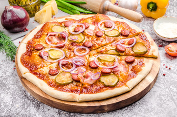 Homemade Meat Loves Pizza with pepperoni sausage, bacon, onions, cucumber, tomatoes, cheese on a wooden board, background, restaurant menu concept. Italian food style, close up.