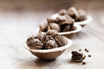Whole black cardamom in coconut bowls on wooden background close-up