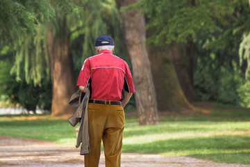 senior walking alone in a park, back view of old man with red shirt 
