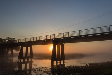 Foggy landscape with a rising sun under the brige across the river.