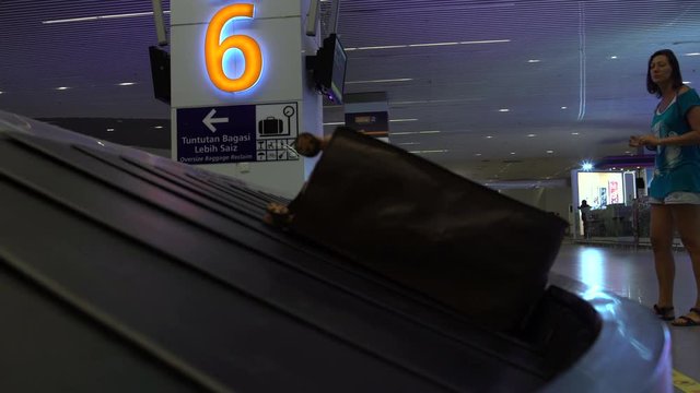 At the airport there is a woman in the waiting room of luggage at the conveyor belt.