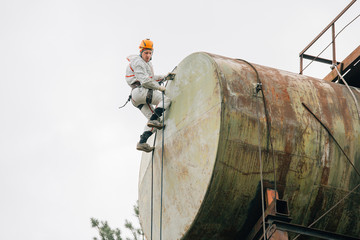 Industrial climber in uniform and helmet working on height outdoors. Professional worker doing his...