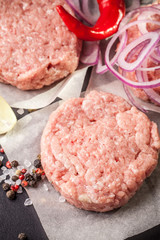 Cutlets from raw minced pork, lamb, veal or beef on parchment. Nearby spices and vegetables. On a black and wooden background. Copy space