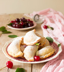 Pies with cherries, sprinkled with powdered sugar and berries of fresh cherries on a wooden surface.