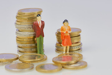 Miniatur Figur: Mann und Frau vor Euro Münzstapel als Symbol für den höheren Verdienst des...
