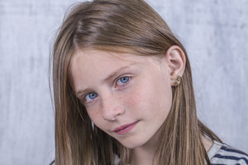 Beautiful blond young girl with freckles indoors on white wall background, closeup portrait