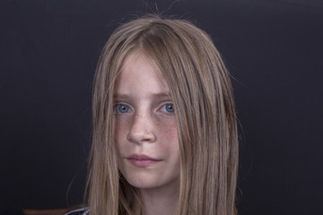 Naklejka premium Beautiful blond young girl with freckles indoors on black background, closeup portrait