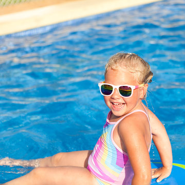 Happy little girl is floating on board in pool