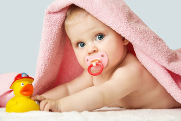 Studio portrait of adorable baby girl covered with pink towel and playing with yellow rubber duck