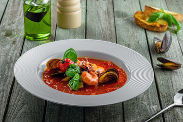 Plate of tomato seafood soup on a rustic wooden table. Tasty Italian classic meal.