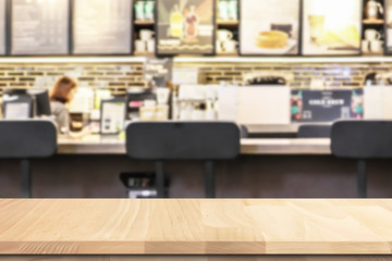 Closeup on beech wooden table top perspective with blurry interior coffee shop scene with bright light for background use.