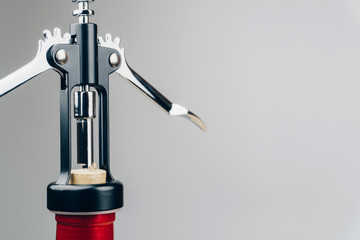 close up of a metal corkscrew with a bottle of red wine