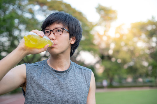 Young Asian man runner drinking energy drink after running in the park