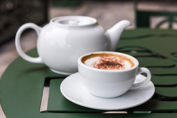 Cappuccino cup with tea pot on green table