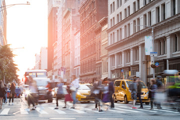 People in motion across a busy intersection in New York City with sunlight background