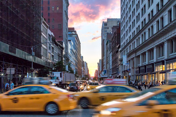 Yellow taxi cabs speeding down Broadway during rush hour in Manhattan, New York City with colorful sunset sky in the background