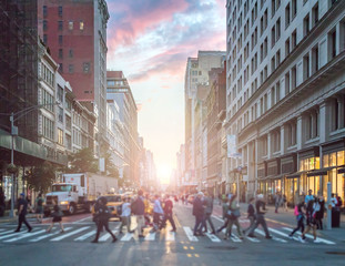 Crowds of people crossing an intersection in Manhattan, New York City with the colorful light of sunset in the background
