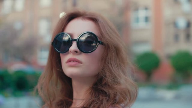 Young beautiful fashionable woman wearing stylish black round sunglasses, posing in street