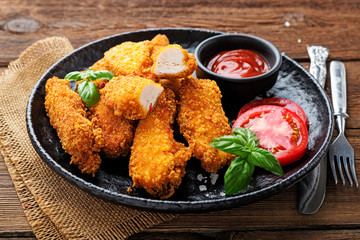 Fototapeta premium Delicious crispy fried breaded chicken breast strips with ketchup on black plate.