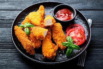 Delicious crispy fried breaded chicken breast strips with ketchup on black plate.