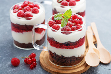 Layered dessert with raspberries,chocolate biscuit cake and cream cheese on a gray background.