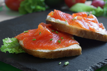 Two sandwiches on toast with soft cheese, fish and greens