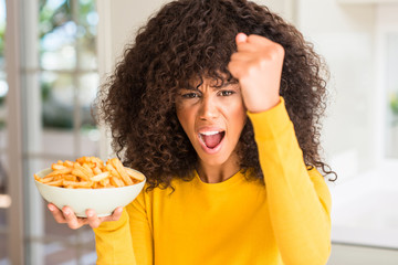 Fototapeta na wymiar African american woman holding a plate with potato chips at home annoyed and frustrated shouting with anger, crazy and yelling with raised hand, anger concept