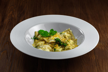Ravioli filled with ricotta, mint and grated lemon rind on a rustic wooden table. Classic Italian cuisine pasta meal in a soup plate.