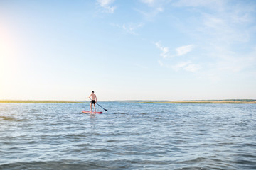 Man paddleboarding on the lake during the morning light, wide landscape view with blue water and sky