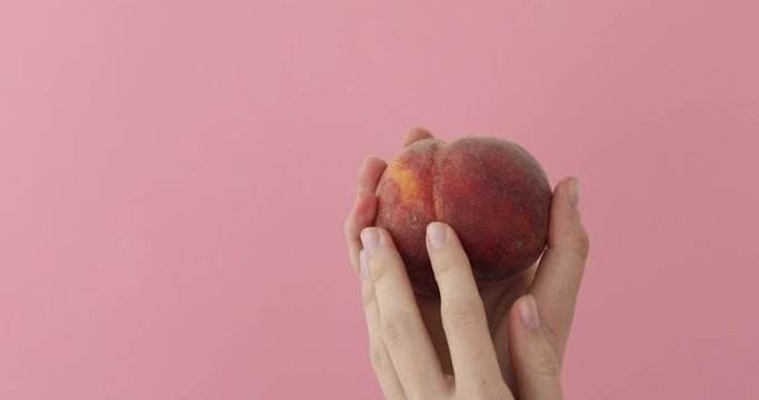 Female hand stroking a peach imprinting a petting close-up on a pink background