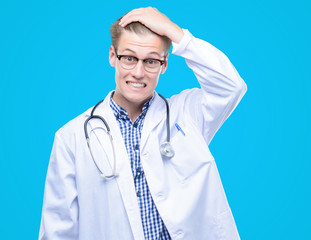 Young handsome blond doctor stressed with hand on head, shocked with shame and surprise face, angry and frustrated. Fear and upset for mistake.