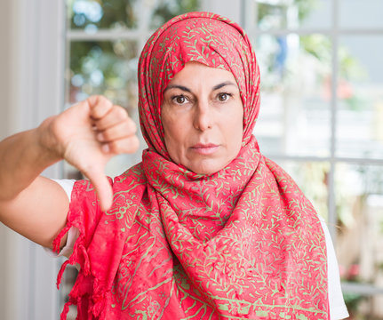Middle aged muslim woman wearing hijab with angry face, negative sign showing dislike with thumbs down, rejection concept