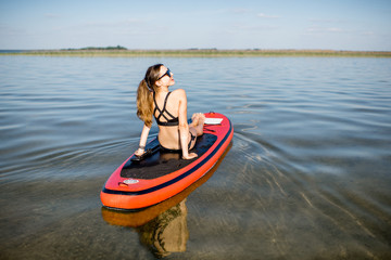 Young woman relaxing on the paddleboard enjoying calm water during the sunset