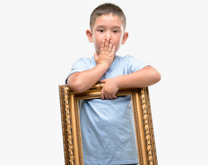 Fototapeta premium Dark haired little child holding frame cover mouth with hand shocked with shame for mistake, expression of fear, scared in silence, secret concept