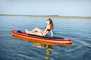 Fototapeta premium Młoda kobieta relaks na paddleboard, ciesząc się spokojną wodą podczas zachodu słońca