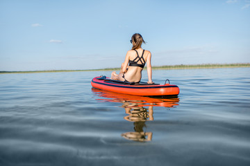 Young woman relaxing on the paddleboard enjoying calm water during the sunset