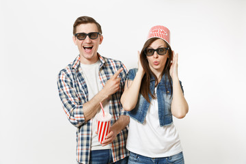 Young happy funny couple, woman and man in 3d glasses with bucket for popcorn on head watching movie film on date, holding plastic cup of soda or cola isolated on white background. Emotions in cinema.