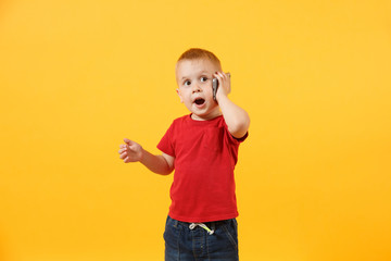 Little kid boy 3-4 years old in red t-shirt talking on mobile phone, conducting pleasant conversation isolated on yellow background. Kids childhood lifestyle concept. Problem of children and gadgets.