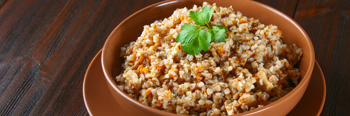 Boiled buckwheat in a bowl with pieces of chicken meat and cilantro on a brown wooden table.